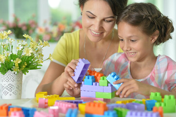 little daughter and mother playing with colorful plastic blocks at home