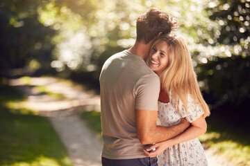 Loving Couple Hugging As They Walk Along Countryside Path In Summer Together