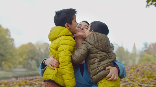 Adorable little boys kissing beautiful young mother outdoors