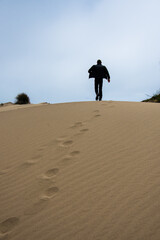 jeune homme marchant de dos de manière décidé sur la crête d'une dune de sable avec ses empreintes de pas visibles dans le sable