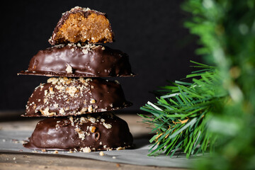 Chocolate covered greek melomakarona with walnuts, placed one on top of each other, next to the christmas tree