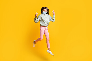 Full size photo of brunette hair kid jump show v-sign wear blue face mask isolated on vivid yellow color background