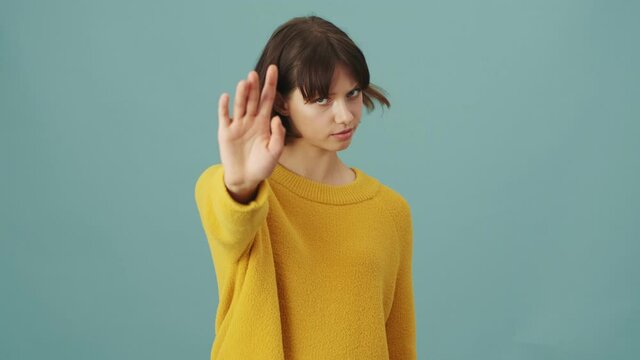 A serious woman is doing stop gesture standing isolated over a blue background in the studio