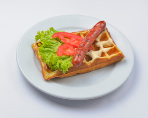 Sour waffle with fried sausage and vegetables on a plate. Delicious traditional breakfast idea. Belgian waffle recipe.