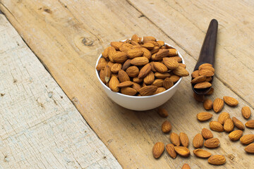 Almond nuts in white bowl with a wooden spoon on wooden background, copy space.food vegetarian.