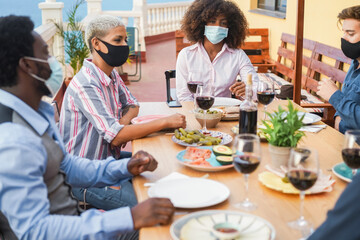 Young multiracial people eating and drinking together while wearing face protective masks - Focus on black girl