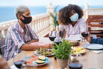 Young multiracial friends eating and drinking wine together at home during coronavirus outbreak - Social distance concept - Focus on black girl