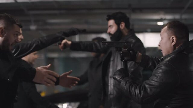 Medium closeup of multi ethnic mobsters at underground parking armed with guns fighting and swearing while leaders aiming pistols at each other looking angrily