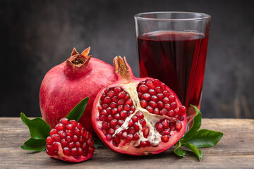 Healthy pomegranate drink in a transparent glass near ripe open pomegranate fruits on a dark...
