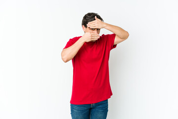 Young cool man blink at the camera through fingers, embarrassed covering face.