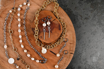 Fashionable gold and silver chains necklace with pearls, earrings on wooden stands.Concrete background with copy space. 