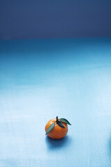 One fresh tangerine with leaves lies on a blue wooden table. Vertical photo with empty space on top for text