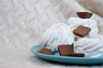 Handmade marshmallows and pieces of milk chocolate on a pale turquoise plate against a background of a knitted cream sweater. New Year. Winter. Christmas