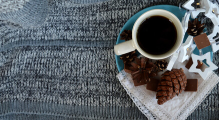 Milky ceramic cup on pale turquoise plate with white lace shawl, milk chocolate pieces, pine and spruce cones and wooden white stars