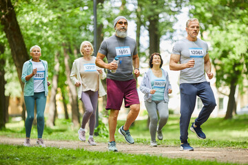 Obraz premium Long shot of healthy senior men and women taking part in marathon race in forest park on summer day