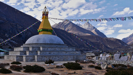 Buddhist stupa (religious monument) in a valley near Thame, Khumbu, Himalayas, Nepal with prayer flags flying in the wind and a wall of mani stones with carved mantras.