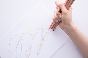 female hand holding wooden colorful pencils and drawing on paper on light background, close view. High quality photo