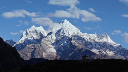 Beautiful panorama of majestic mountain Thamserku (peak: 6,623 m) with the silhouettes of a small temple and Buddhist prayer flags in foreground near Thame, Khumbu, Himalayas, Nepal.