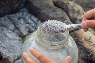 Hands pouring fresh wood ash into a glass jar