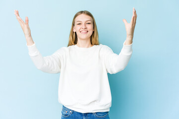 Young blonde woman isolated on blue background celebrating a victory or success, he is surprised and shocked.