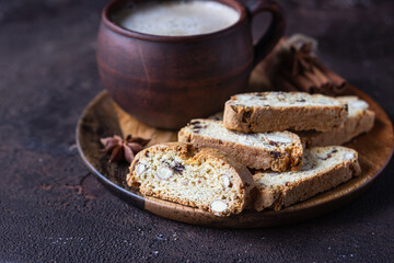 Wooden plate with traditional Italian cookies and a cup of coffee. Biscotti or cantucci with almond and raisin. Brown stone background.