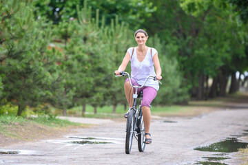 Naklejka premium Girl riding a bicycle on a rainy warm summer morning