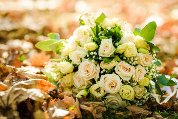 Obraz na płótnie Canvas Wedding bouquet made of white and yellow roses. Wedding bouquet on the ground surrounded by autumn leaves.