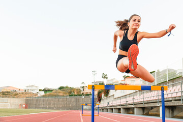 Fit female teenager athlete hurdler running jumping over hurdles - Copy space