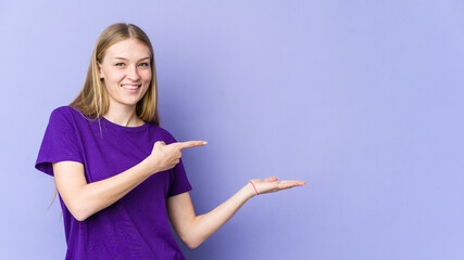 Young blonde woman isolated on purple background excited holding a copy space on palm.