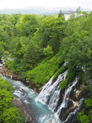 Fototapeta na wymiar Shirogane waterfall in Shirogane onsen in Biei, Hokkaido, northern Japan blue, with turquoise water of pond caused by colloidal aluminium hydroxide