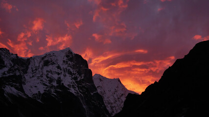 Dramatic sunset with purple and orange colored clouds in the Himalayas with snow-capped craggy mountains near sherpa village Thame, Khumbu region, Nepal on Three Passes Trek.