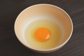 Closeup of a Fresh Raw Egg Yolk and White in a Bowl Isolated on Wooden Table