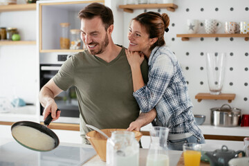 Husband and wife making pancakes at home. Loving couple having fun while cooking..