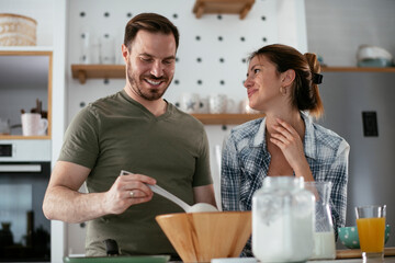 Husband and wife making pancakes at home. Loving couple having fun while cooking..