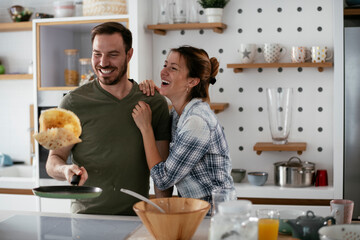 Husband and wife making pancakes at home. Loving couple having fun while cooking..