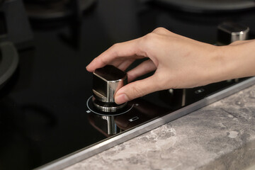 Woman hand turning switch knob on gas stove in kitchen.