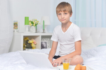 Boy with laptop on bed in the morning