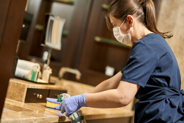 Housemaid in uniform and protective gloves cleaning the hotel bathroom - obrazy, fototapety, plakaty