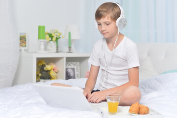 Obraz na płótnie Canvas Boy listening to music on bed while having breakfast
