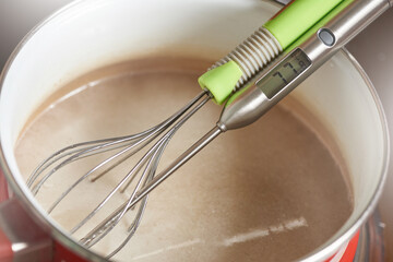 Kitchen measuring cooking thermometer and whisk in a saucepan with hot cream