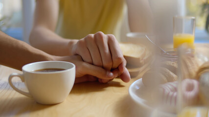 Young cheerful man holding gay partner hand having breakfast in morning