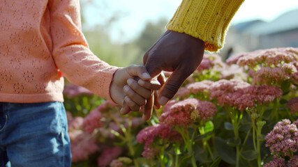 Close up of african father and mixed race child holding hands over flower bush background