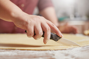 Closeup female hands cutting the raw dough with a knife