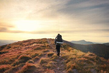 Man backpacker traveling with a dog. Hiker going uphill against scenic sunset sky background