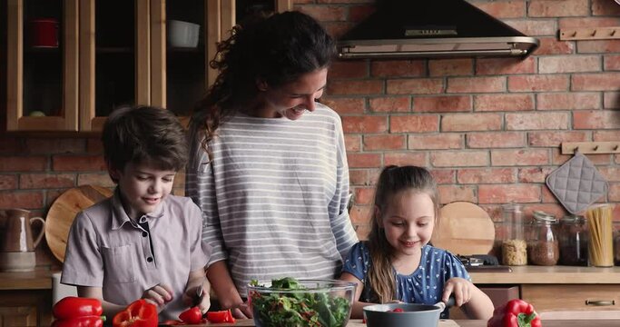 Mom and little 6s 8s kids prepare together salad in kitchen. Mother teach adorable children cooking, share skills develop son and daughter, buy fresh organic ingredients caring about offspring health