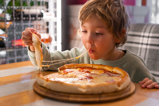 Cute boy eating a piece of pizza at fast food restaurant. Child unhealthy meal concept. Hungry kid