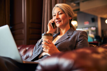 Charming businesswoman talking on cellphone and using laptop