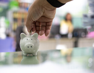 Close up. Hand of a man holding a coin for putting to white piggy bank in the bank office. Money-saving concept investment budget wealth business. Copy space on design, text. Bokeh, blurred background