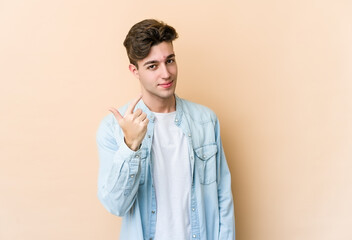 Young caucasian man isolated on beige background pointing with finger at you as if inviting come closer.