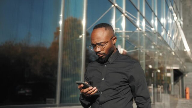 African American Businessman in a suit using smartphone on a street in downtown. Black man smiles and looks successful. Browsing the web on device.